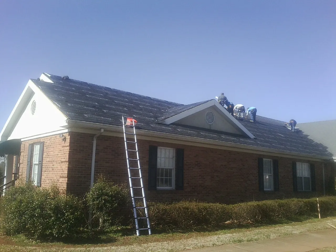 Crew tearing shingles off a brick ranch roof with a ladder set — Metal Roof Repair work by our crew in Jewell