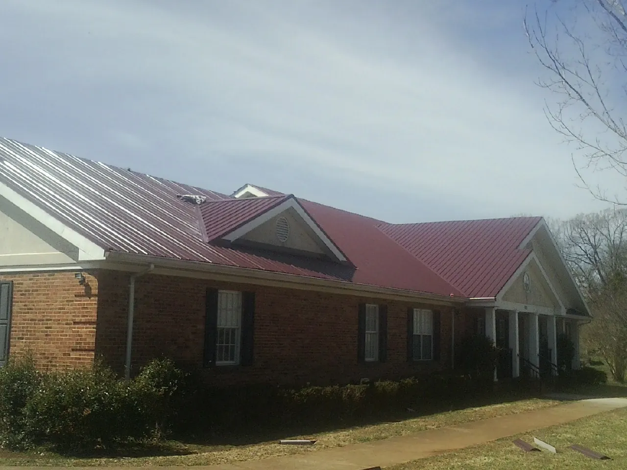 Red metal roof with gabled entries on a long brick building, from a Hail Damage Roof Repair job in Jewell