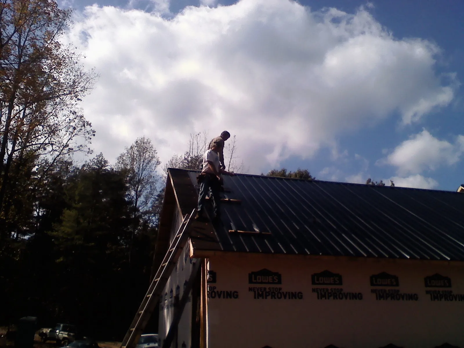 Roofer fastening dark metal panels high against a cloudy sky, from a Roof Inspection job in Jewell