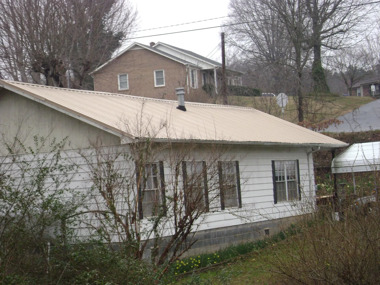 Tan metal roof on a white sided house set into a hillside — Commercial Roofing by Roofing Brothers in Jewell